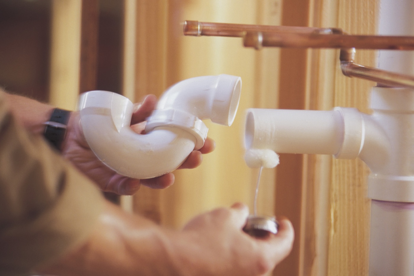 Plumber fitting a PVC drain trap beside copper supply lines